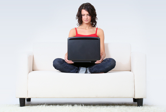 Woman sits on white sofa with black laptop on her lap